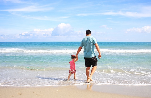 father holding hands with daughter walking in shallow water at beach